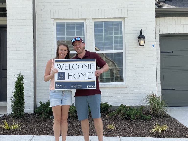 Happy homebuyers holding a Welcome Home sign after buying with The McDonald Group in Dallas-Fort Worth